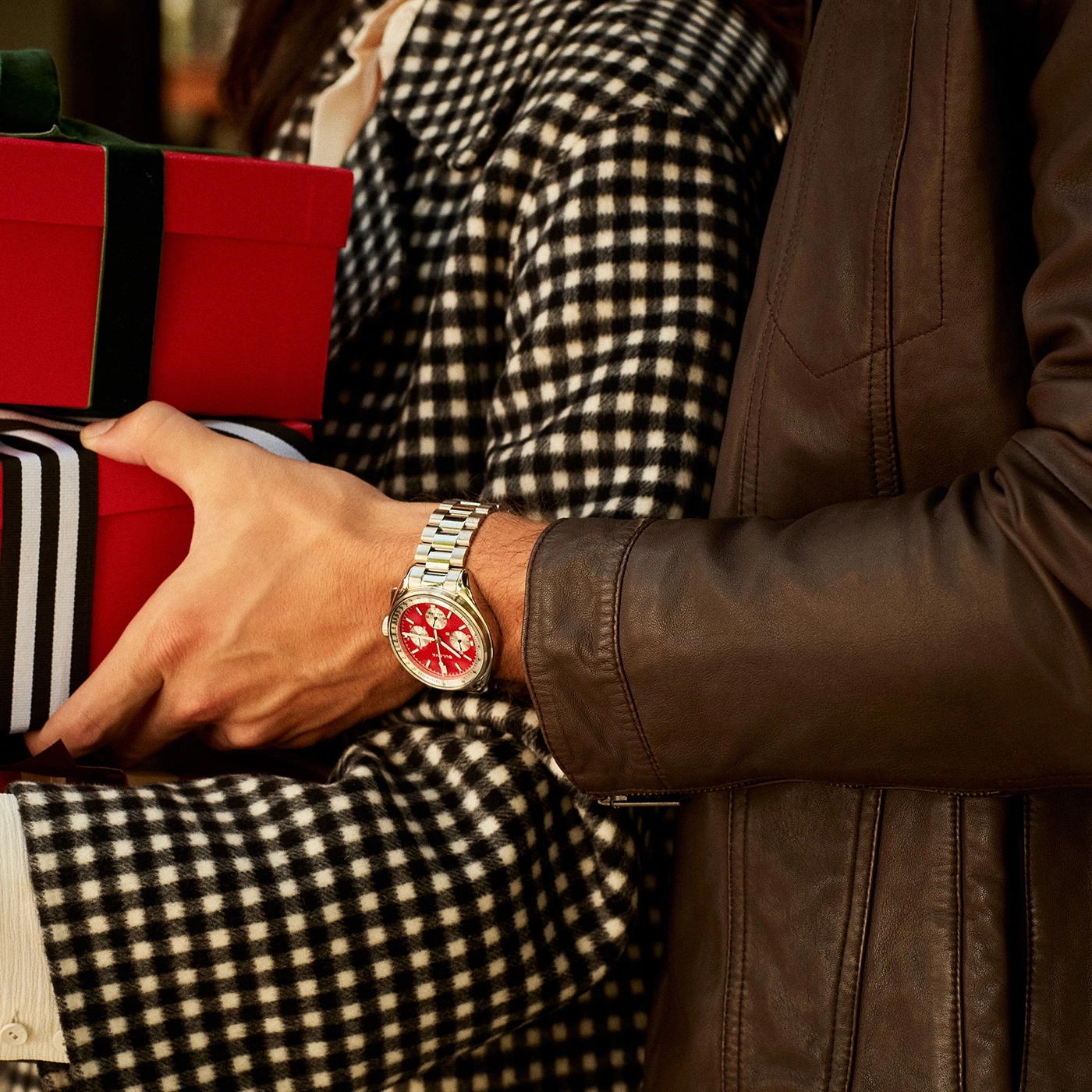 Mann mit Uhr hält Geschenke, Frau im karierten Mantel, Lederjacke