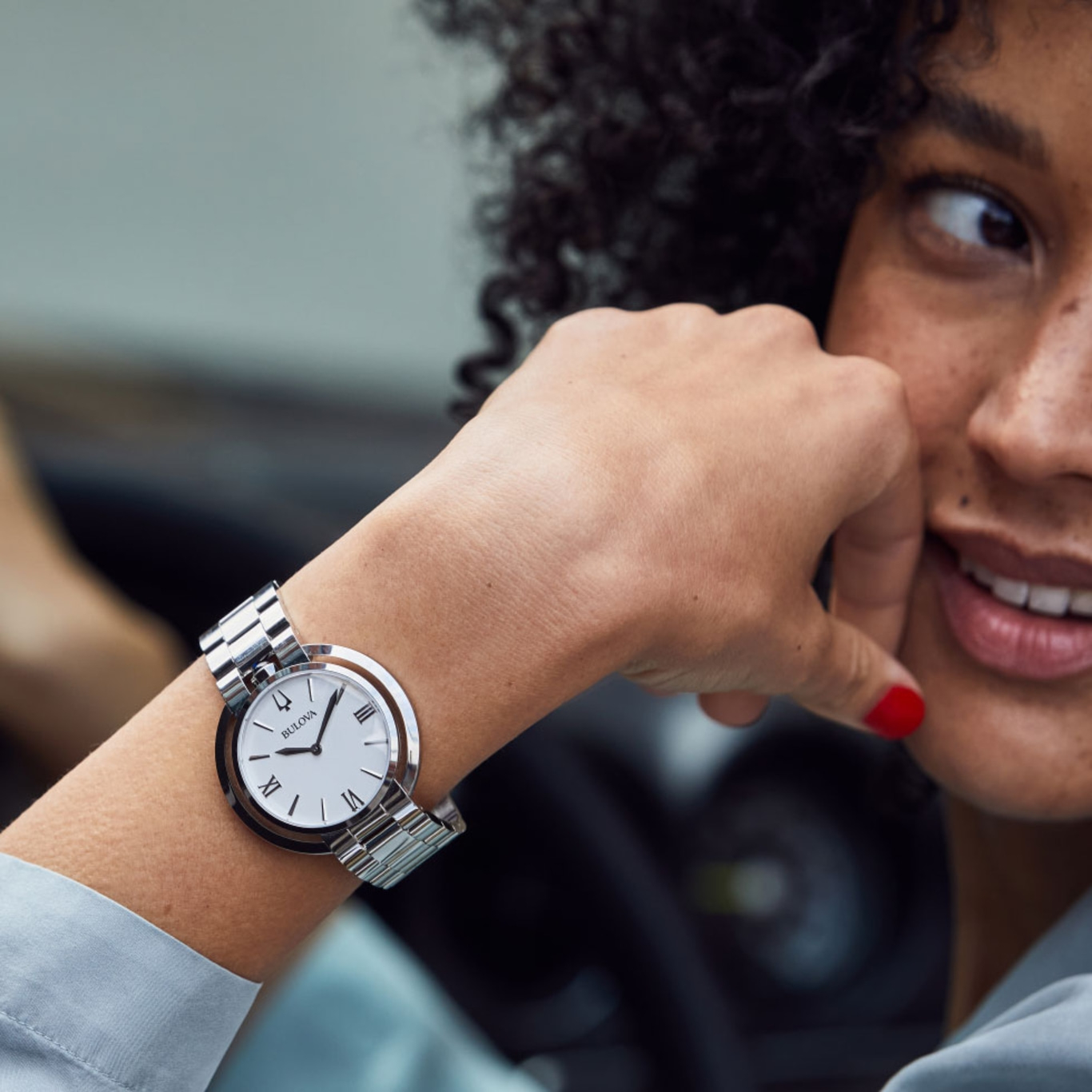 Frau mit Uhr, die sich am Handgelenk befindet, lächelt und in die Ferne blickt.