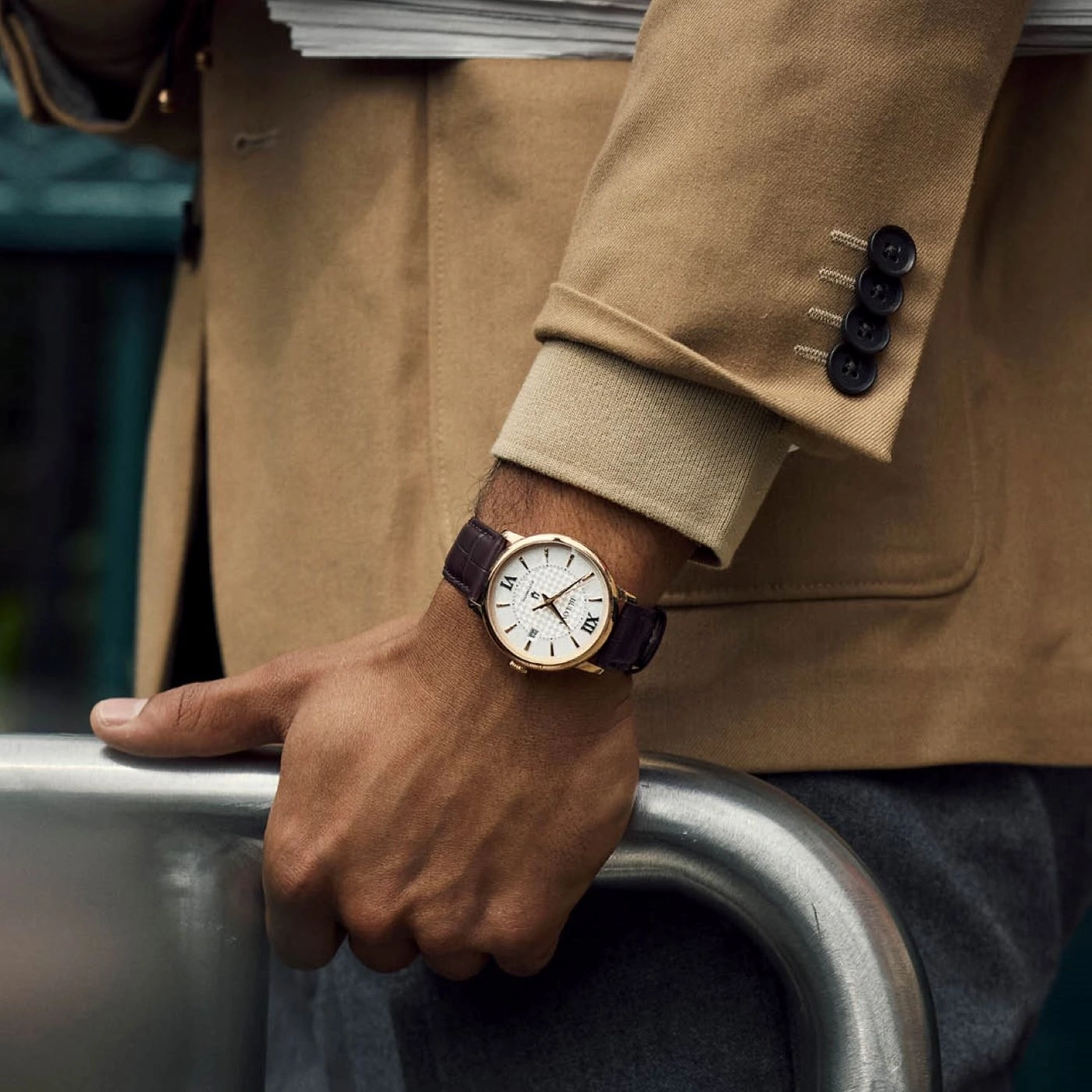 Mann mit Uhr und Jacke, die sich auf einem Metallgeländer abstützen.