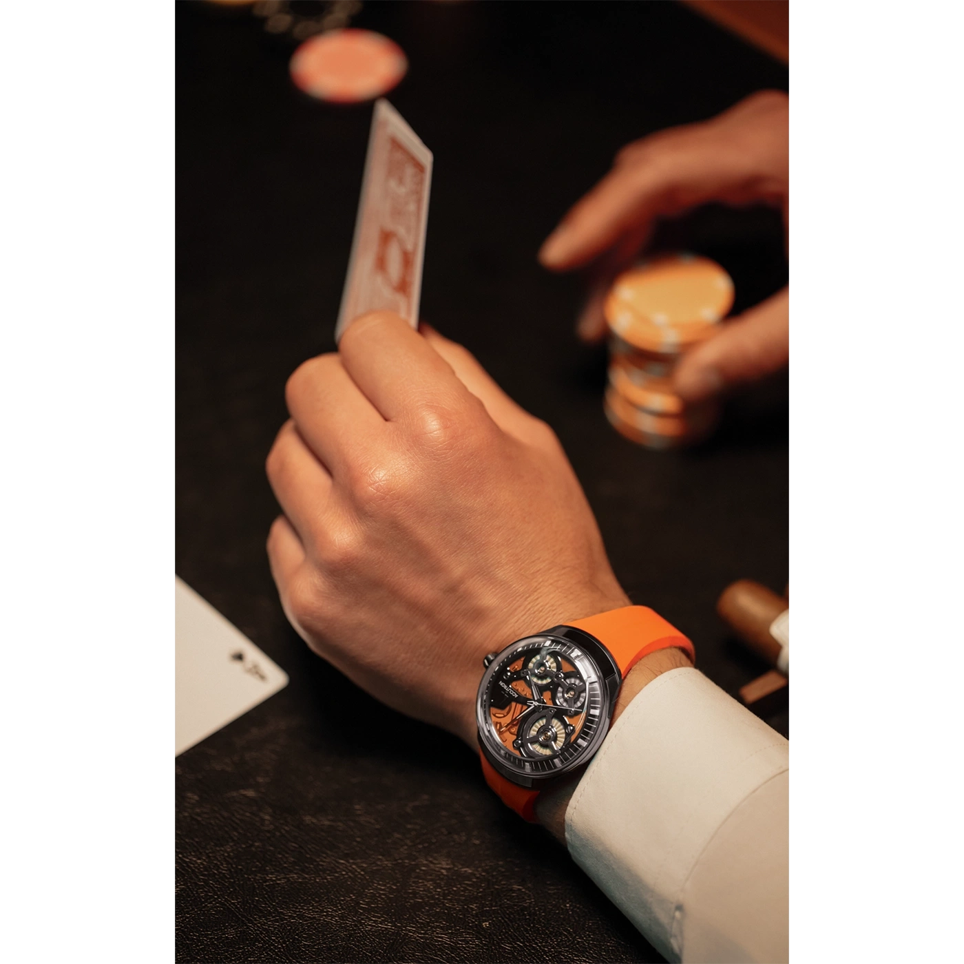 Mann mit Uhr spielt Poker, hält Karten und Chips in der Hand.