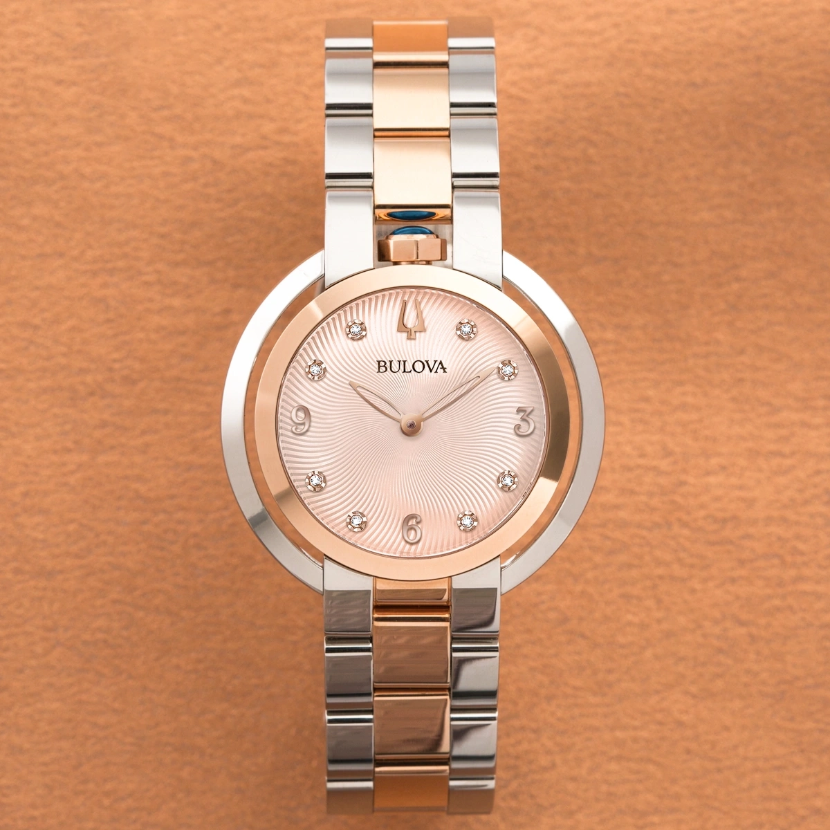 Bulova Damenuhr, rosafarbenes Zifferblatt, Diamanten, goldfarben, silberfarbenes Armband, Lederhintergrund