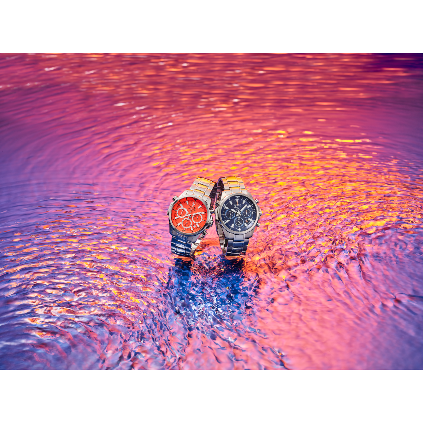 Zwei Uhren auf einer glitzernden, farbenfrohen Wasseroberfläche. Glänzende Armbänder.