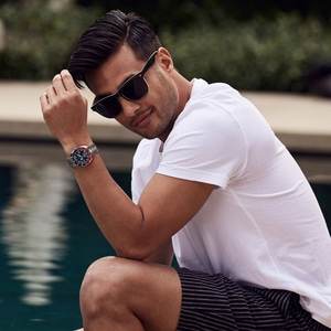 Mann mit Sonnenbrille und Uhr am Pool, lächelt in die Kamera.