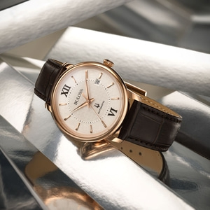Goldene Bulova-Uhr mit braunem Lederarmband auf silbernem Hintergrund.