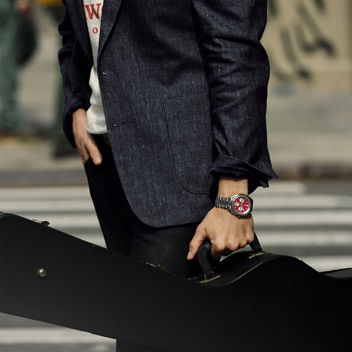 Mann mit Gitarrenkoffer und Uhr, gekleidet in Jacke und Jeans