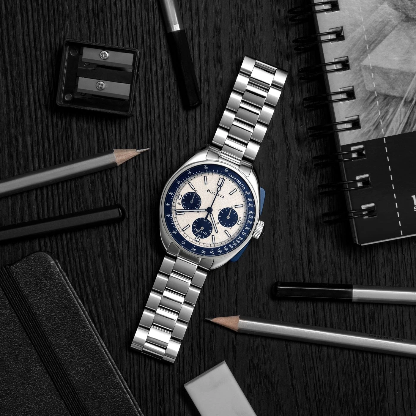 Uhr, Stifte, Notizbuch und Radiergummi auf schwarzem Holz. Bulova-Uhr.