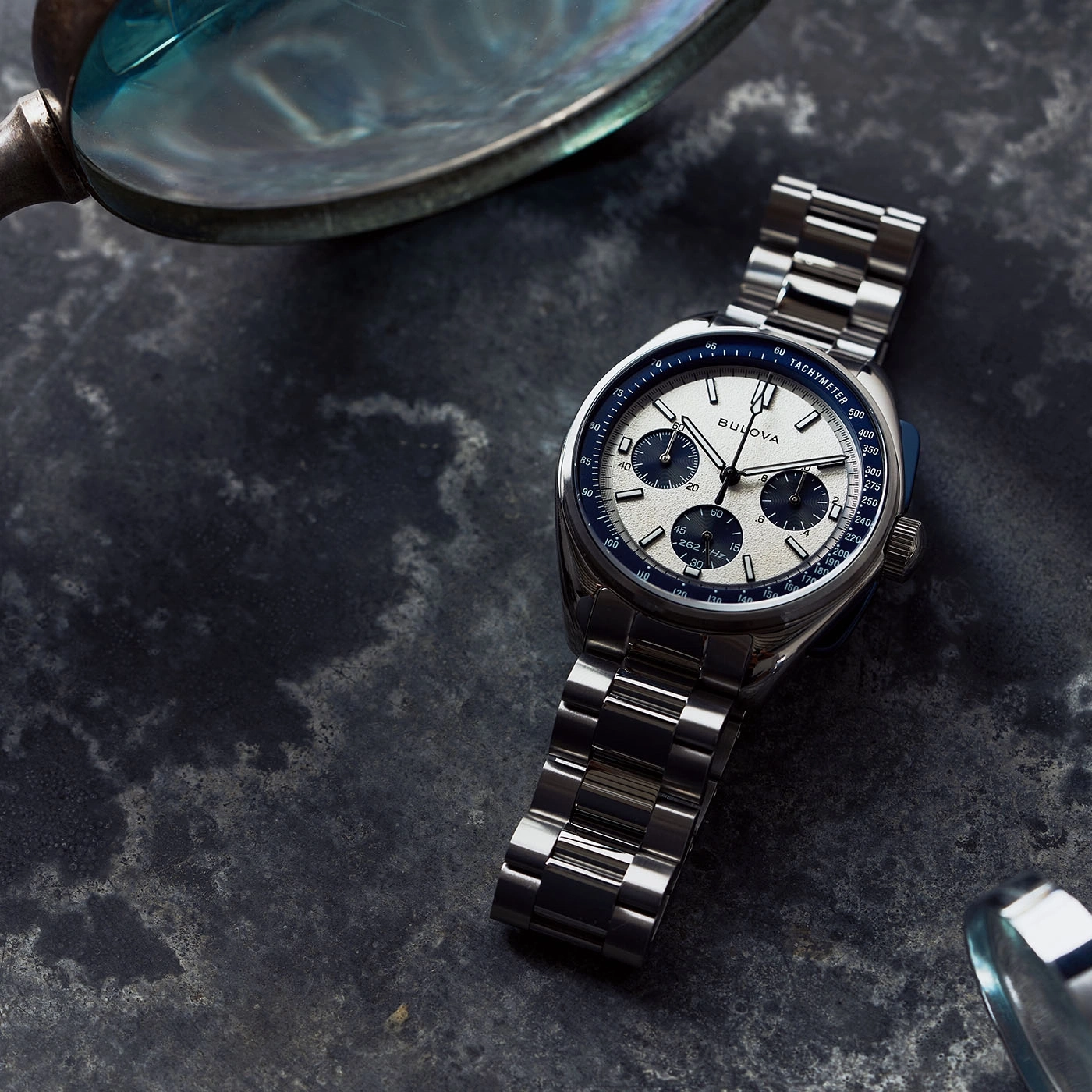 Uhr mit Metallarmband und Tachymeter auf dunklem Untergrund, Nahaufnahme.