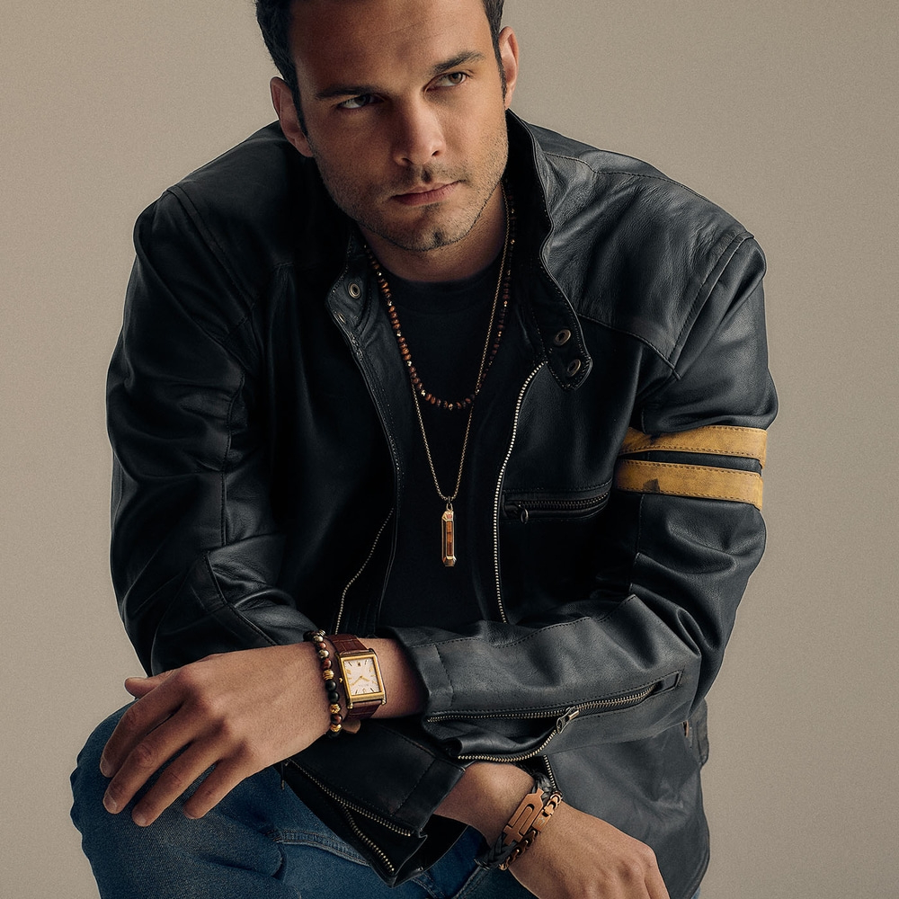 Mann in Lederjacke mit Schmuck und Uhr, Jeans, posiert