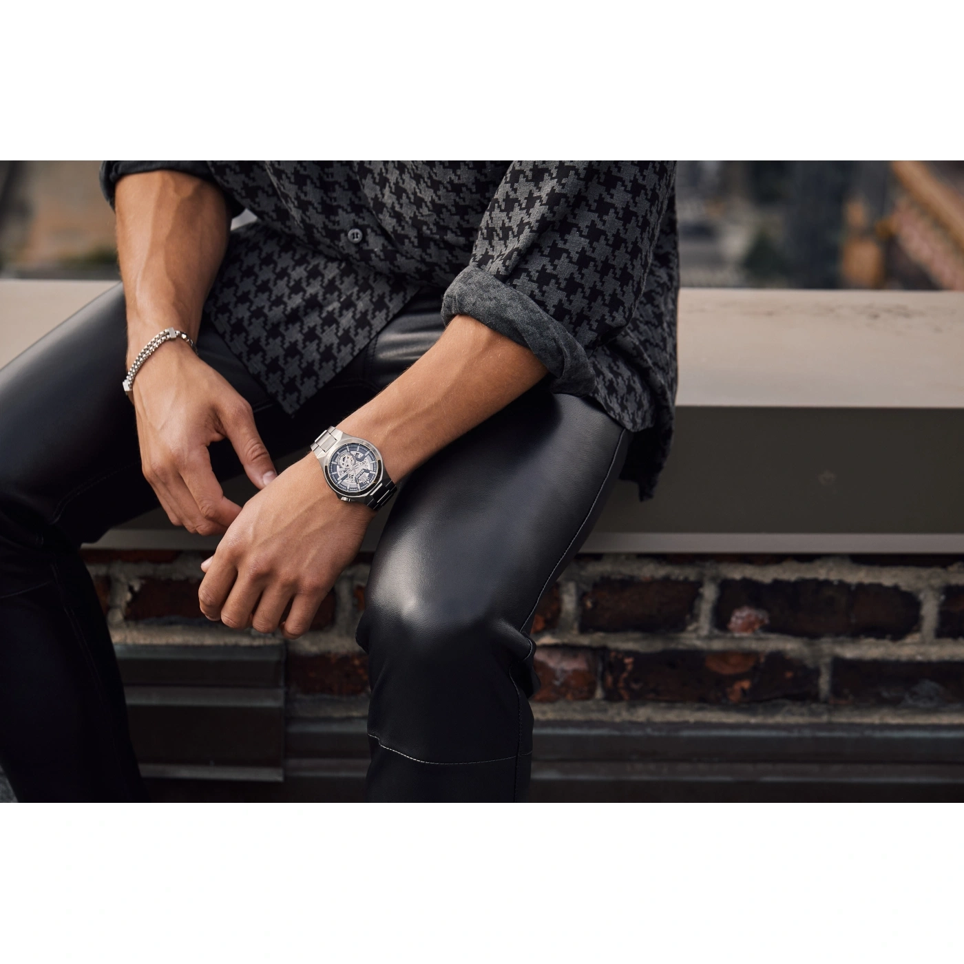 Mann mit Uhr und Armband, sitzt auf einer Mauer, Lederhose, Hemd