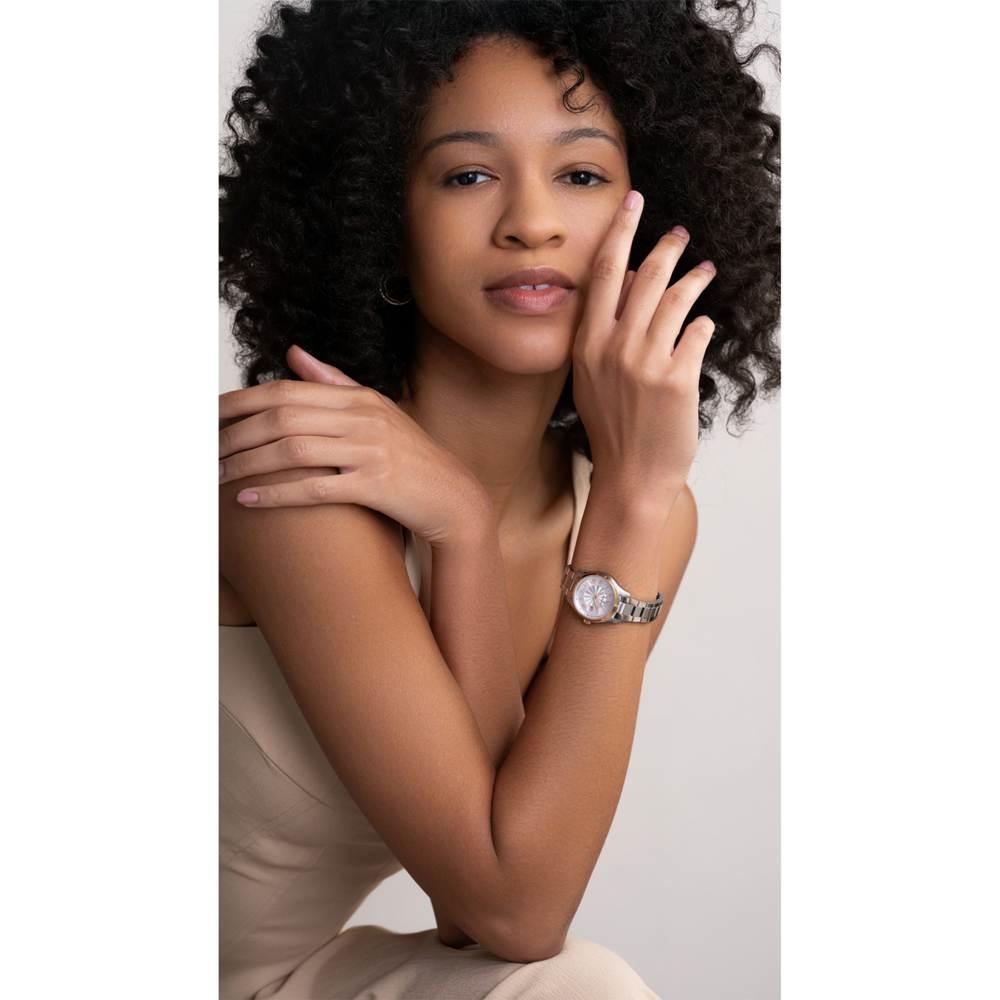 Junge Frau mit lockigem Haar, die eine Uhr trägt und in die Kamera schaut.
