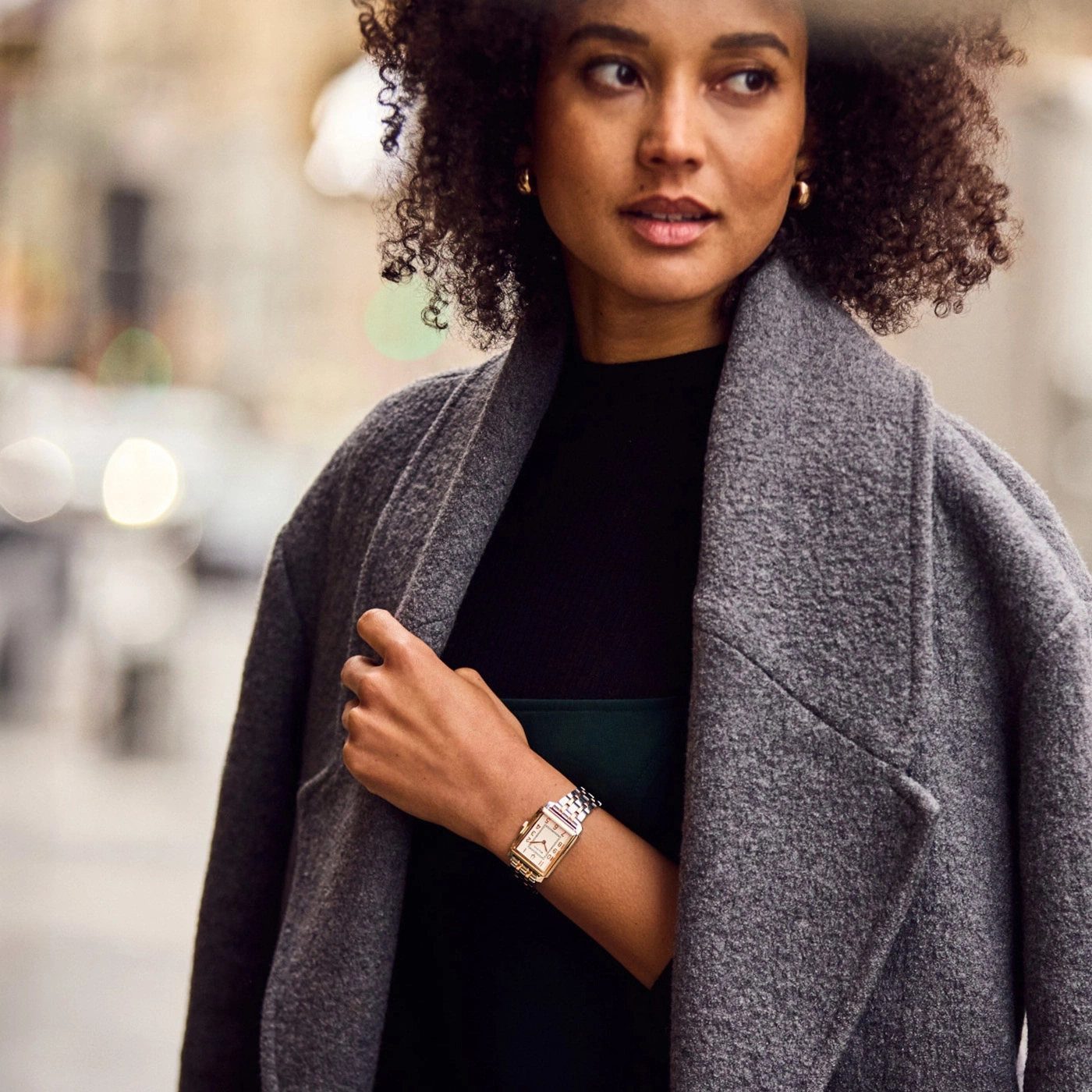 Frau mit Locken und Uhr trägt grauen Mantel