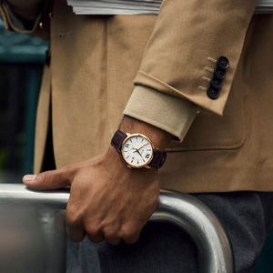 Mann mit Uhr und Jacke, die sich auf einem Metallgeländer abstützen.