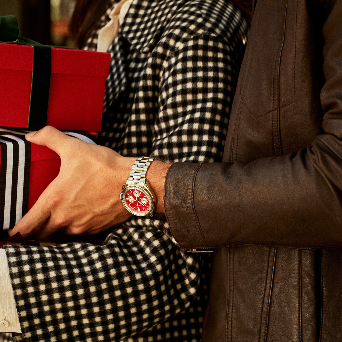 Mann mit Uhr hält Geschenke, Frau im karierten Mantel, Lederjacke