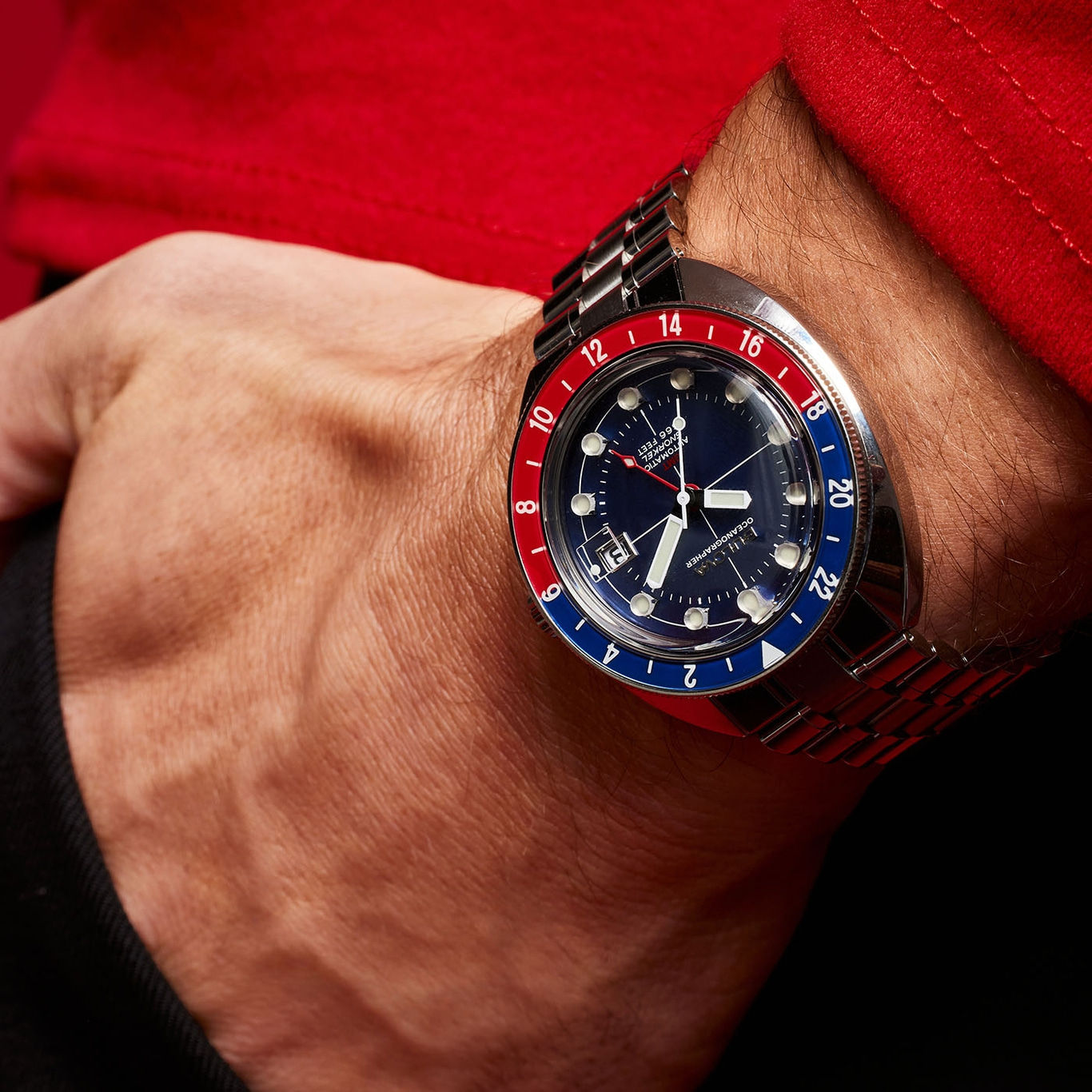 Uhr am Handgelenk mit blauem Zifferblatt und rot-blauer Lünette, Nahaufnahme