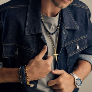 Mann mit Schmuck, Jeansjacke und Uhr. Er hält die Jacke offen.