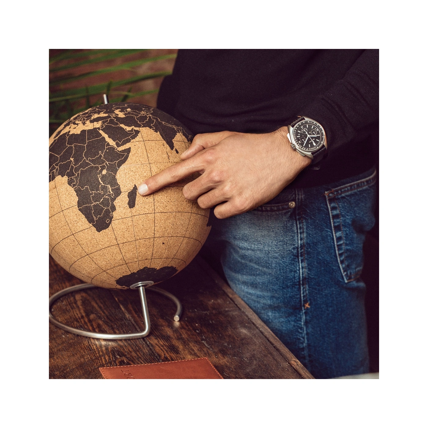 Mann zeigt auf Madagaskar auf einem Globus, trägt eine Uhr und Jeans.