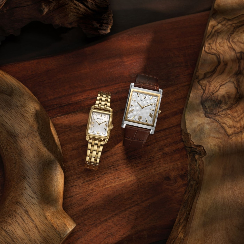 Zwei Bulova-Uhren auf einem Holzbrett, gold und braun, elegant.