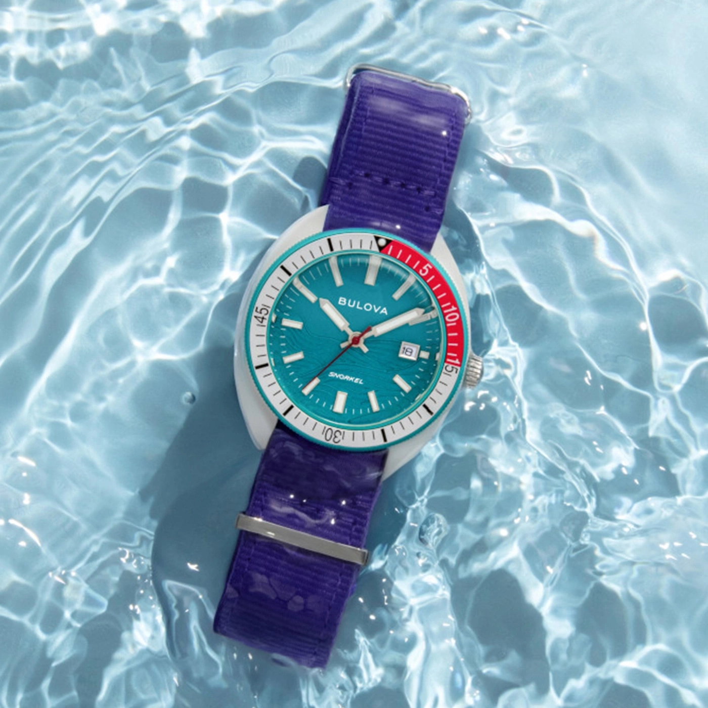 Eine Taucheruhr mit blauem Zifferblatt und lila Band im Wasser.