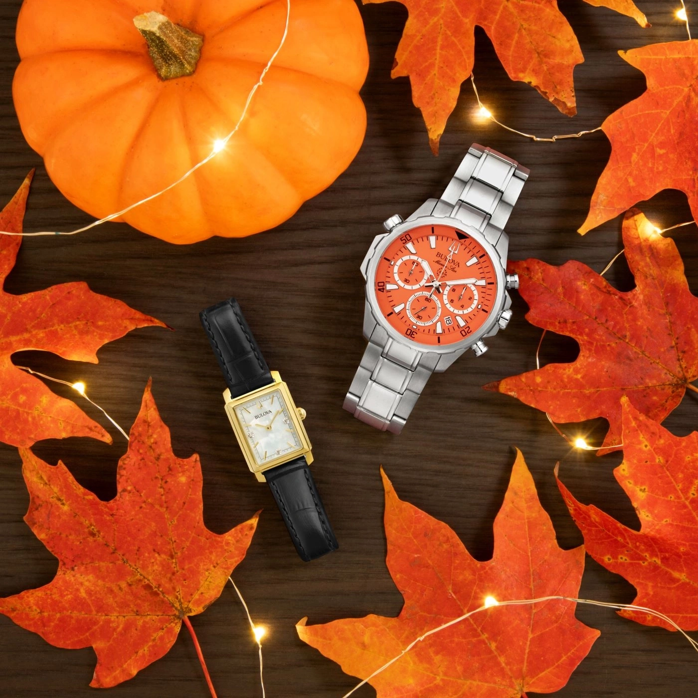 Herbstliche Szene mit Kürbis, Blättern, Uhren und Lichterketten auf Holz